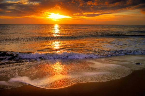A beautiful sunset along Tanjung Aru Beach with orange sky and calm waves

